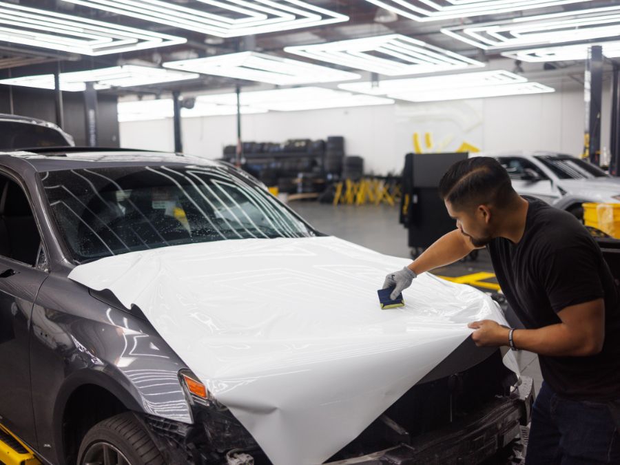 Technician applying a professional car wrap to a white vehicle hood