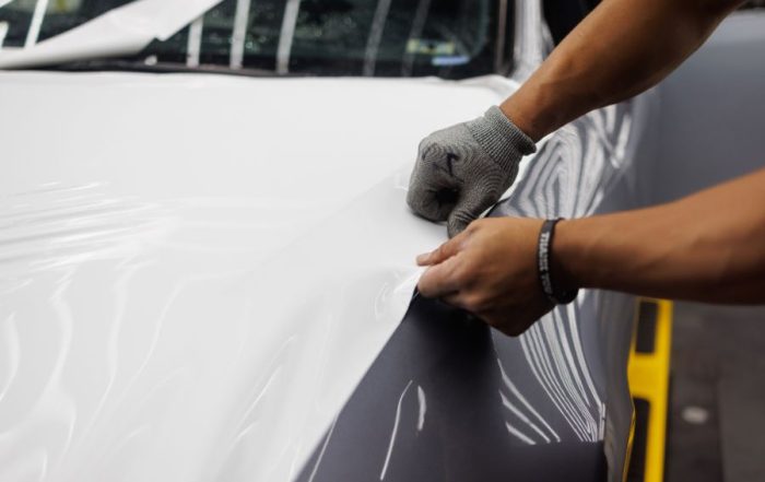Worker applying a white vinyl wrap to a car hood as part of a professional car wrap service