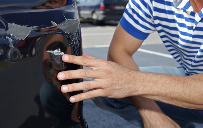 Man inspects car bumper damage, considering paintless dent removal in Arizona